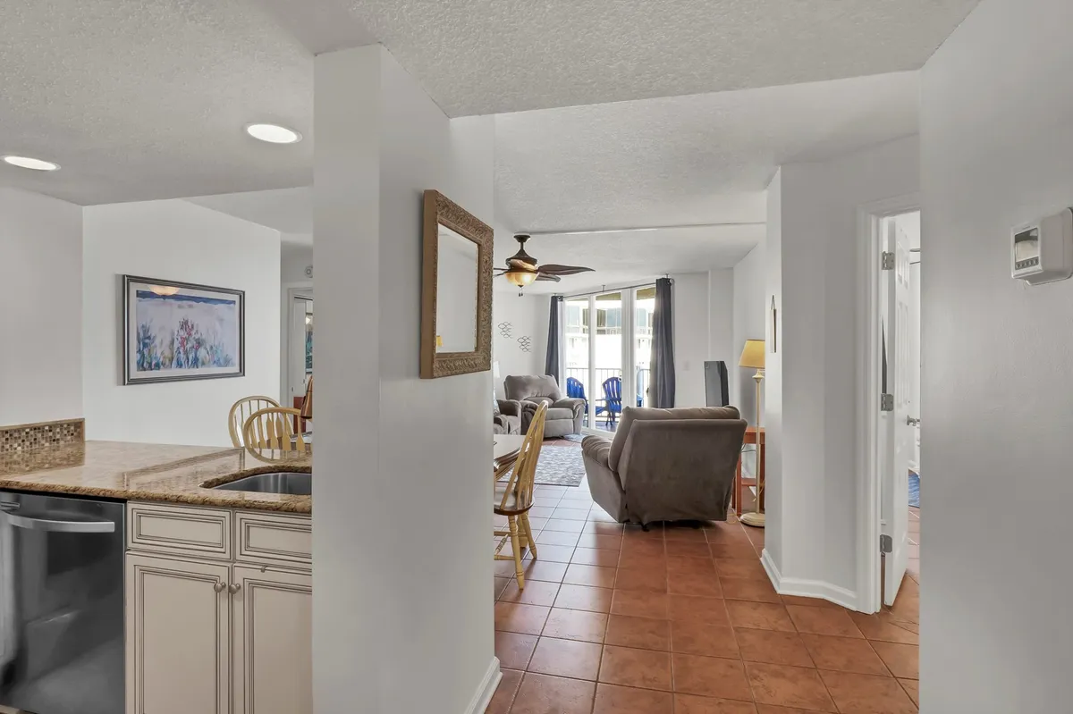 This photo features a kitchen counter that opens up to a seating area, bathed in natural light from the windows, highlighting the open-concept design. The kitchen is integrated into the broader living space, supporting a sense of connection and shared activity.