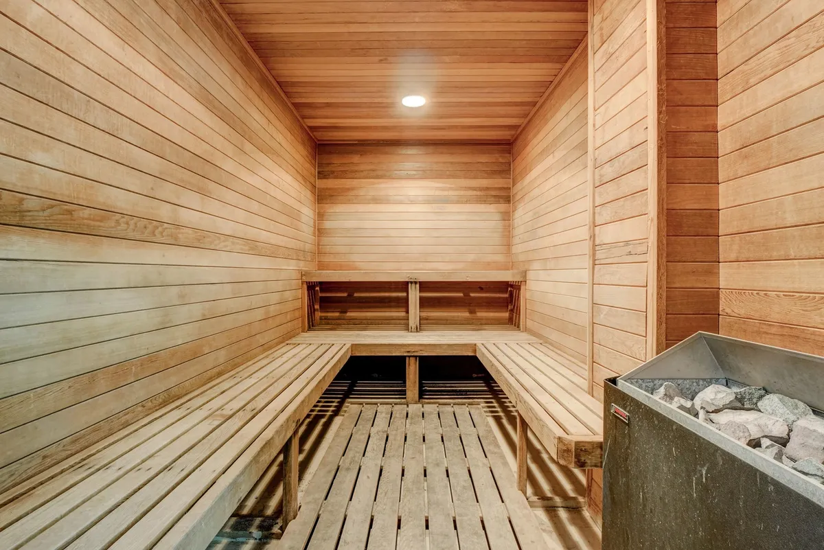 A tranquil sauna space clad in wood, featuring stone heaters and wooden benches. The ambiance is soothing, evoking relaxation and wellness rituals shared among friends or couples.