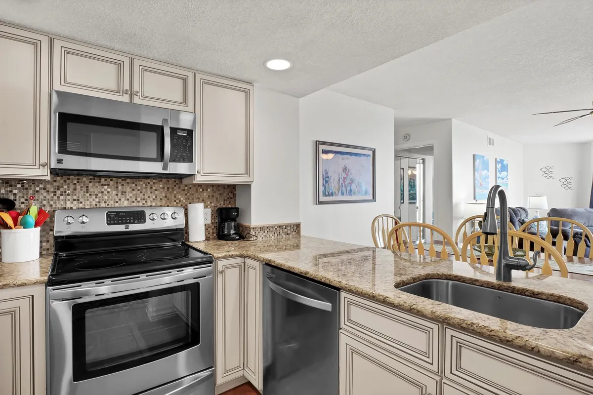 This image shows a bright, modern kitchen with stainless steel appliances, granite countertops, colorful kitchen utensils, and lively wall art. The space is clearly designed for cooking and entertaining, with a layout that feels open and inviting.