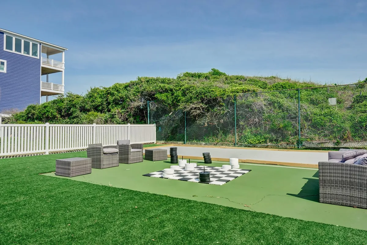 A playful outdoor scene centered around a large chessboard, with comfortable seating and lush greenery in the background. The space is set up for friendly games, social interaction, and enjoyment of the outdoors.