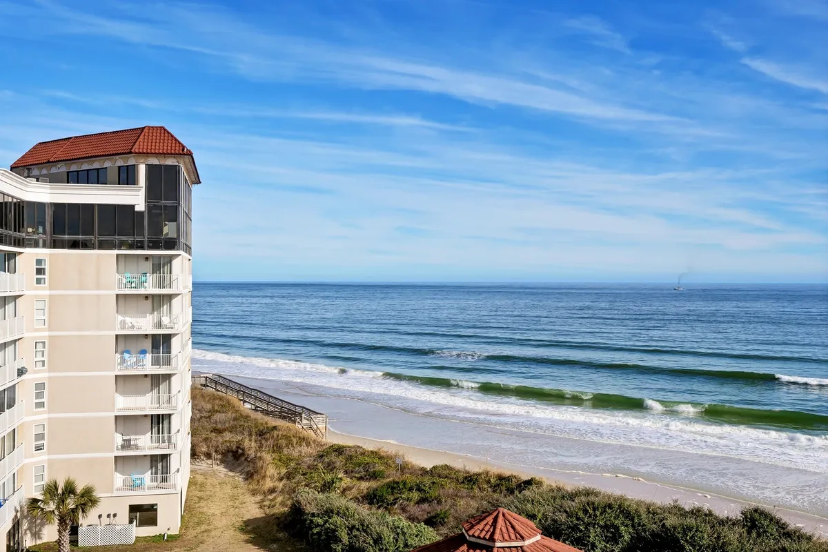 The image shows a stunning oceanfront view with gentle waves rolling onto a wide sandy beach, just steps away from the St Regis residential building. The inviting scene features a relaxing mood, perfect for beach walks, sunbathing, and watching the sunrise over the Atlantic.