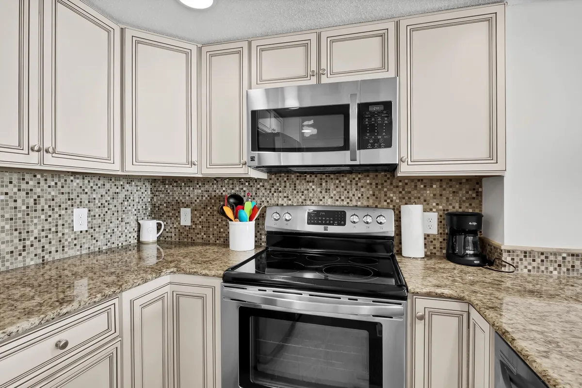 A close-up of the renovated kitchen area, showing stainless steel appliances, a pristine granite countertop, and a colorful utensil holder. The inviting mood suggests a space ready for both daily use and special occasions.