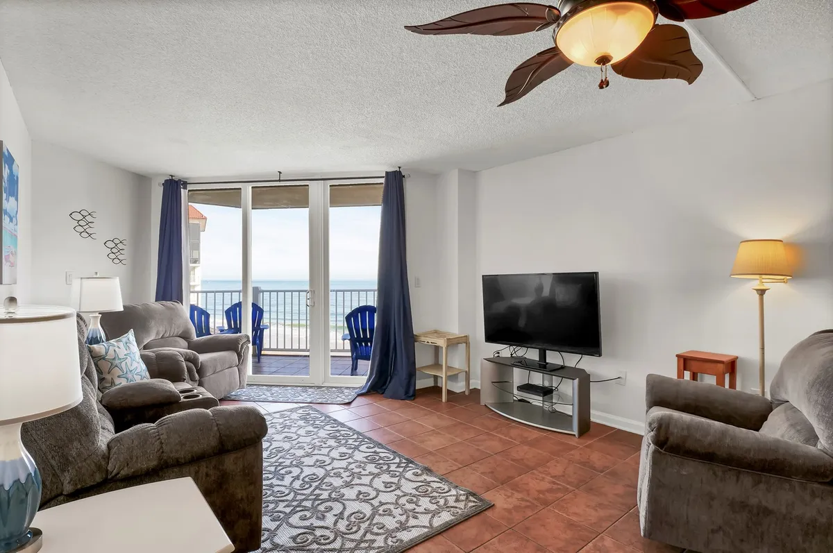 A comfortable seating area is bathed in sunlight, with plush chairs and a decorative lamp arranged to maximize enjoyment of the sweeping ocean views through large windows. The relaxed layout invites both solo relaxation and group gatherings while emphasizing the ever-present seascape just outside.