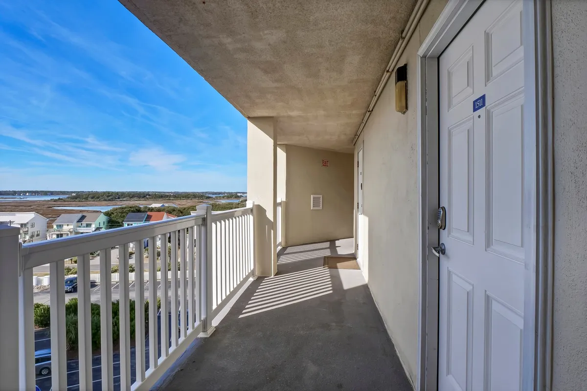 An inviting exterior view of a balcony with a railing, looking out over landscaped grounds. The scene suggests moments of relaxation after activities, as well as the proximity to outdoor amenities and the beach.